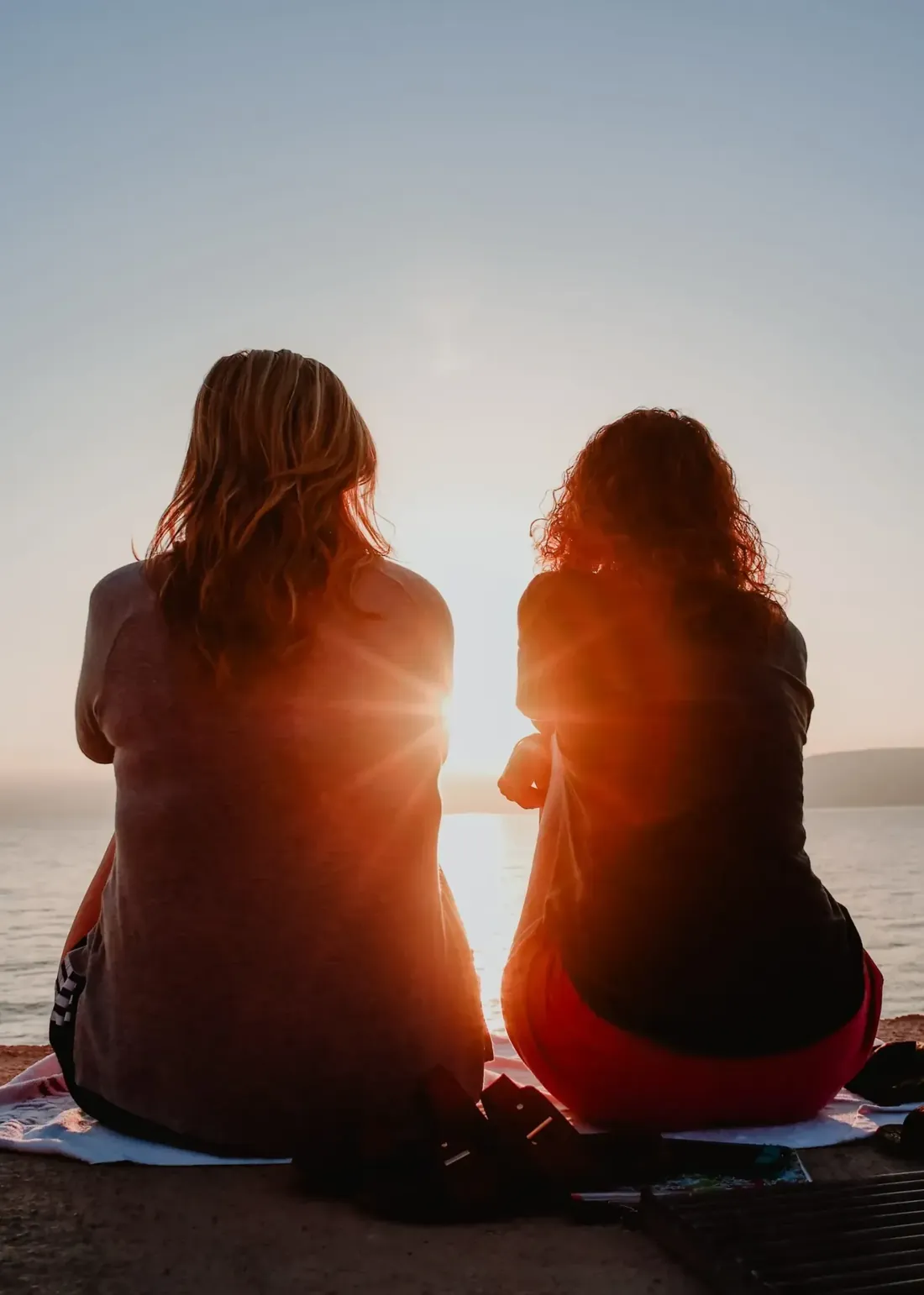 Two friends sitting side by side, watching the sun set over the water