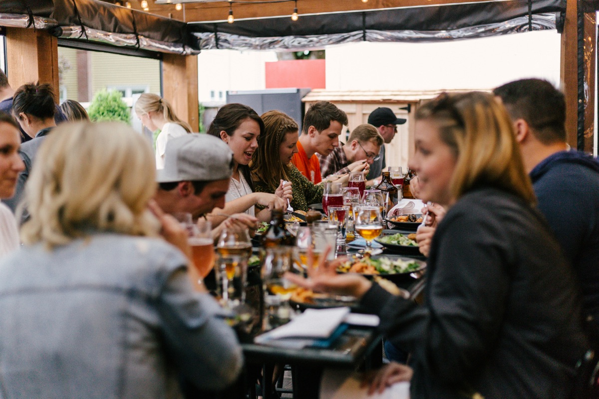 Friends talking over dinner and drinks at a long table on a restaurant patio
